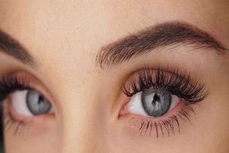 Woman brushing through clean eyelashes with a mascara wand, demonstrating proper lash care technique