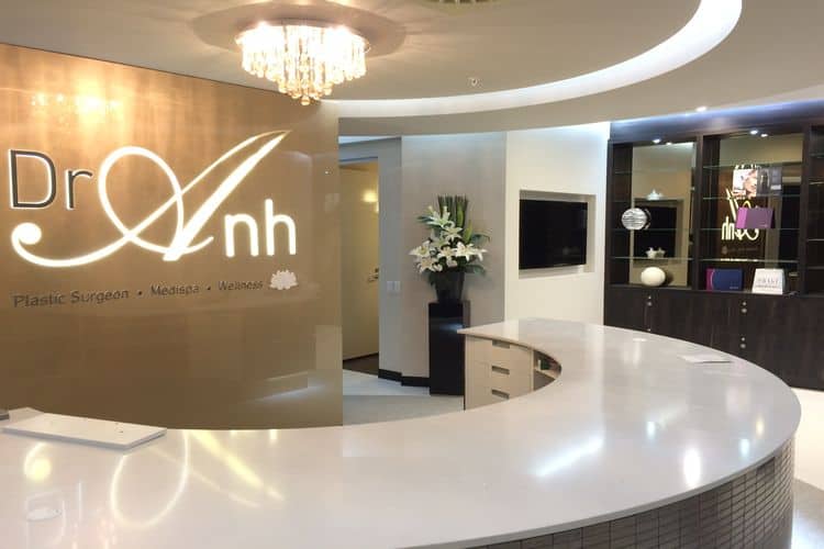 Reception area at Dr Anh medispa in Perth with curved white desk, crystal chandelier, branded feature wall and warm ambient lighting