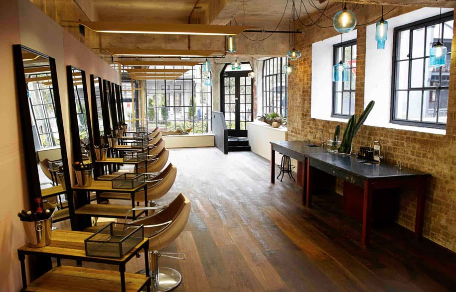 Modern industrial-style hair salon interior with dark wood panels, exposed brick, and low-hanging pendant lights