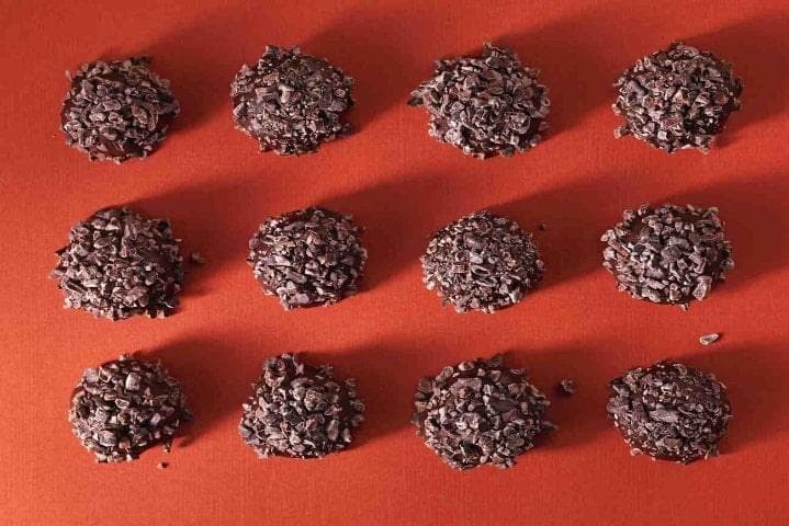 Artfully arranged raw cacao nibs, cacao butter and dark chocolate pieces on marble surface with fresh berries