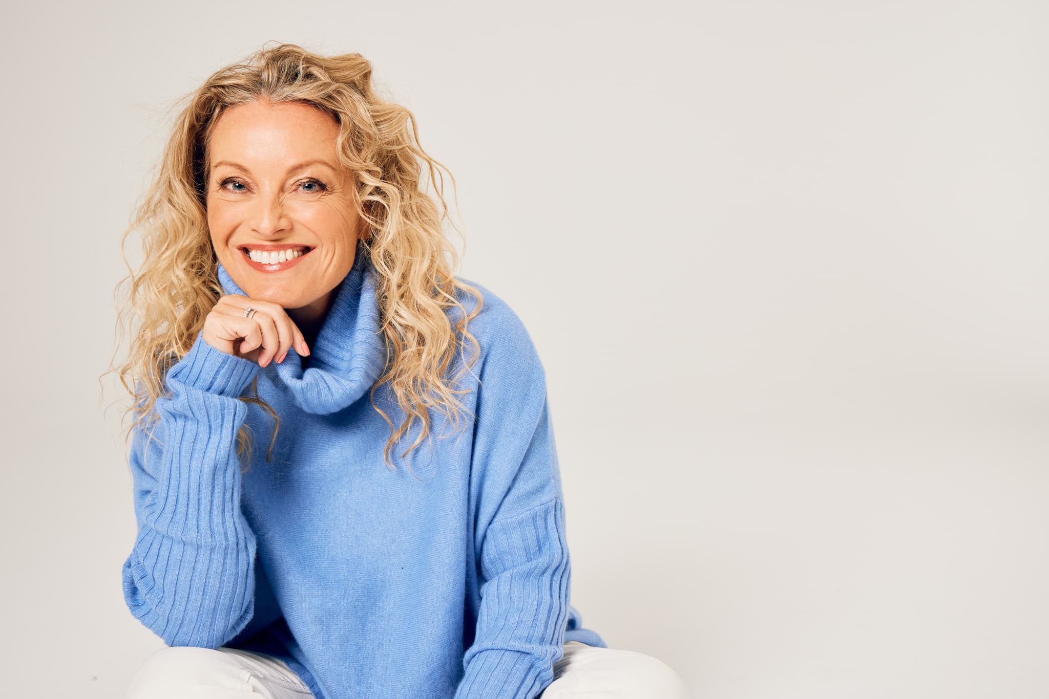 Lisa Walker, co-founder of Eir Women, sitting cross-legged in a blue turtleneck sweater