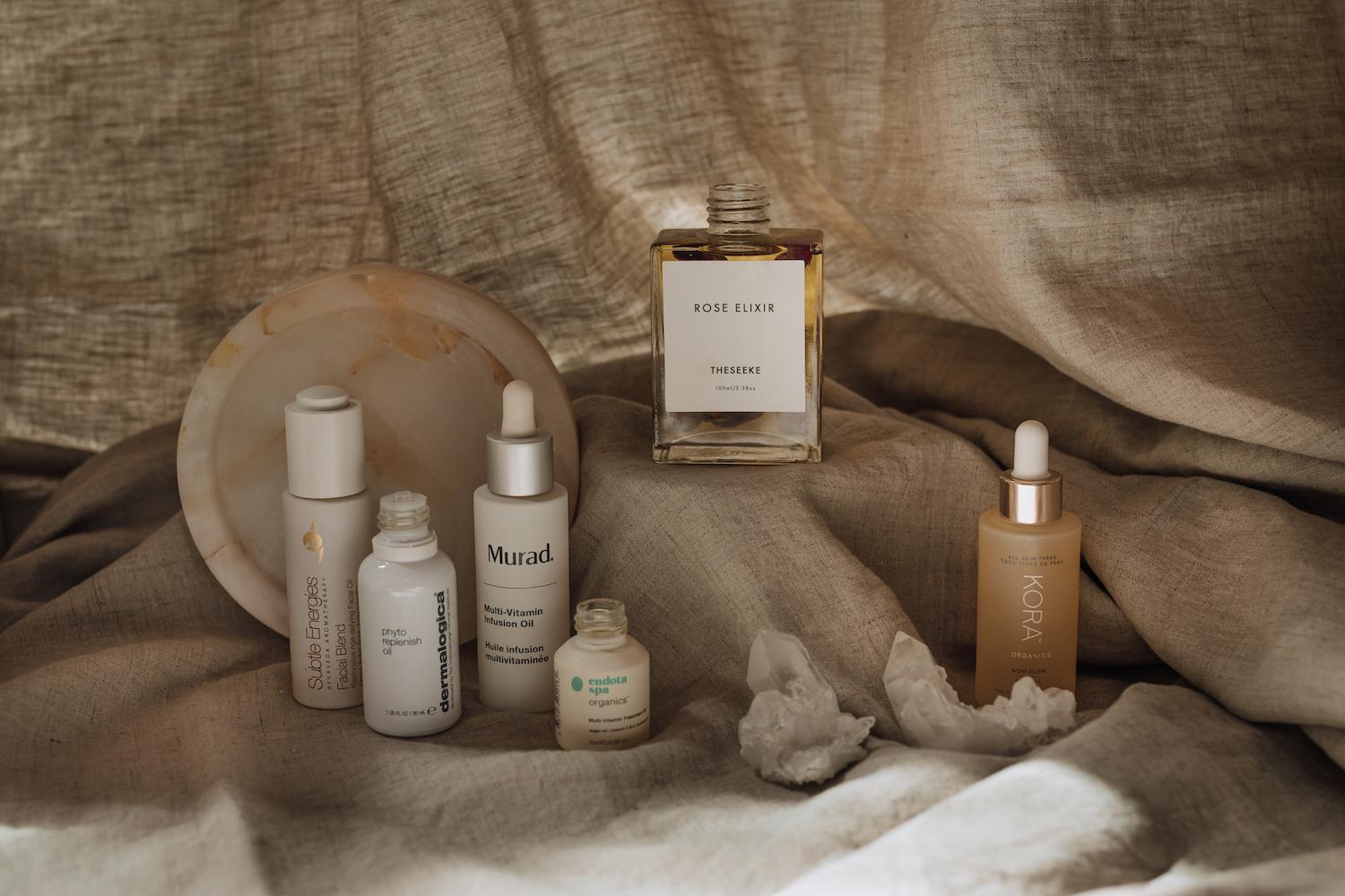 Luxury facial oils in glass bottles arranged on marble surface with winter botanicals and rose buds