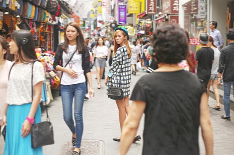 Colourful K-beauty storefronts and shopfronts lining a busy pedestrian street in Myeongdong, Seoul, with illuminated brand signage for skincare retailers.