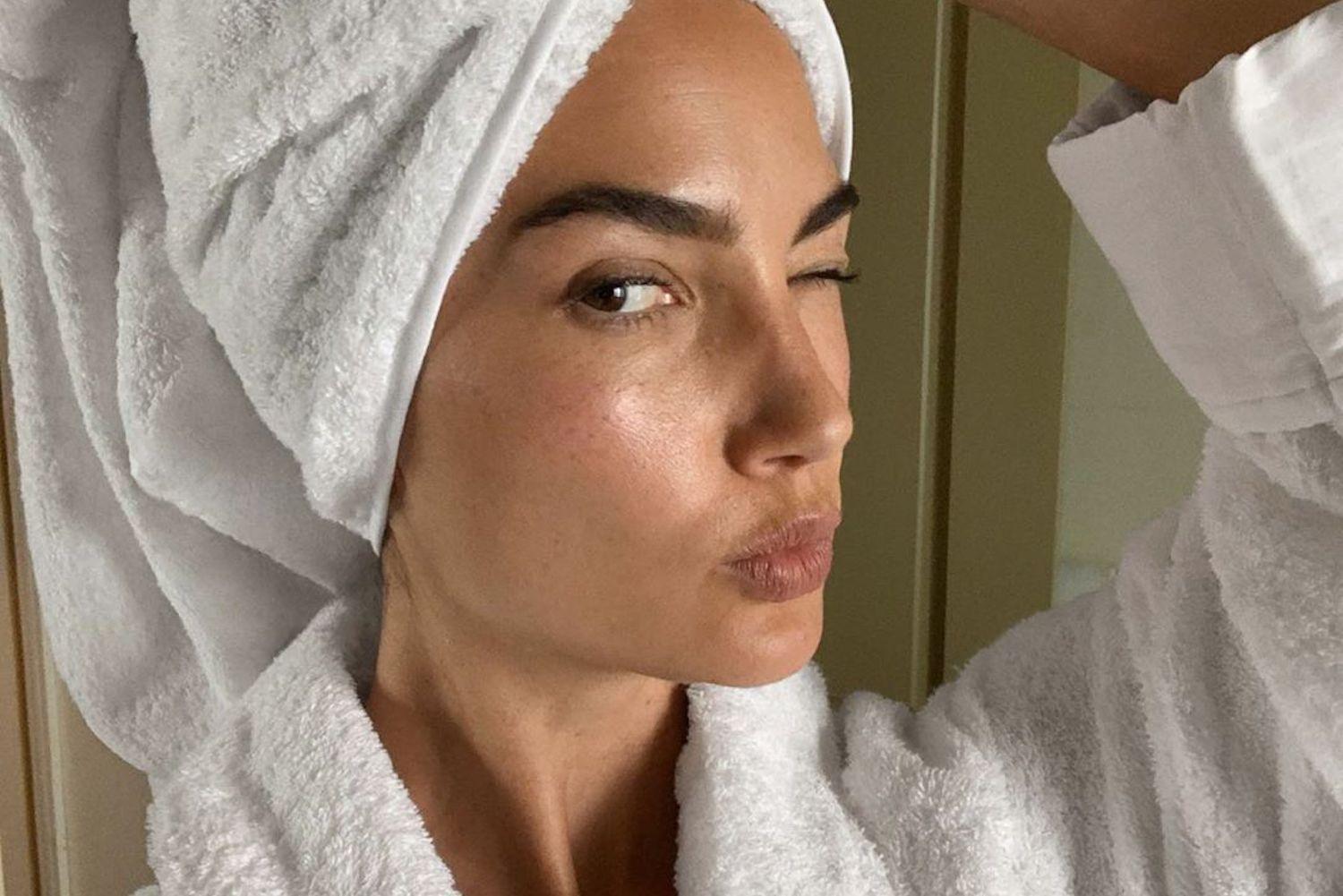 Woman applying face mask during home skincare routine with vitamin A serum and sunscreen nearby
