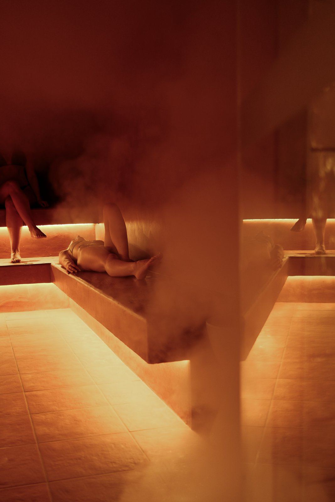 Steam drifting over amber-lit stone benches in the steam room at 38° The Bathhouse, Bondi Beach