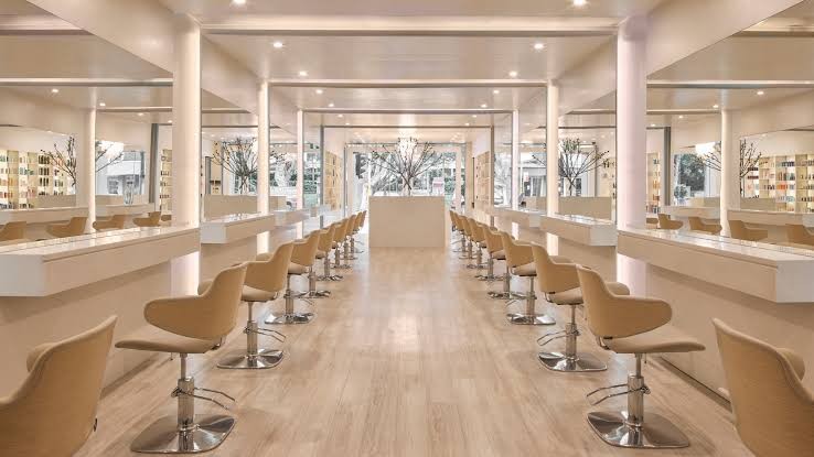 Long salon floor with white styling stations, beige chairs and potted trees at Paloma, Paddington