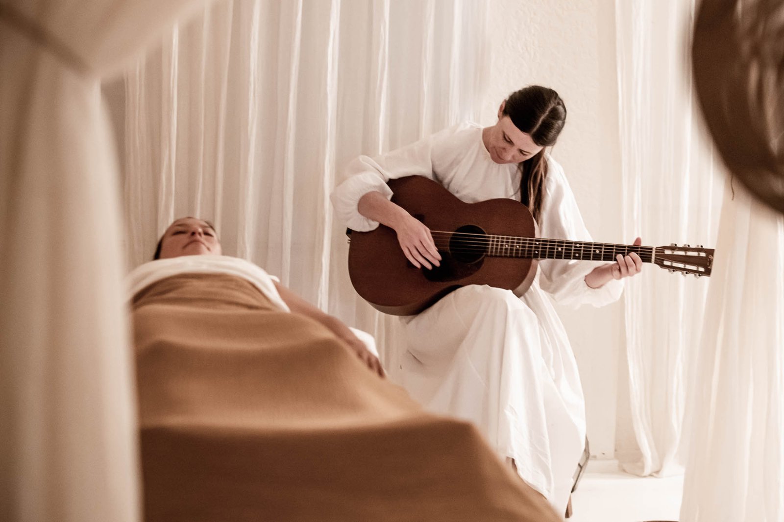 A practitioner plays guitar beside a guest resting on a treatment bed during a sound healing session at Chakana Day Spa + Wellbeing, Avalon