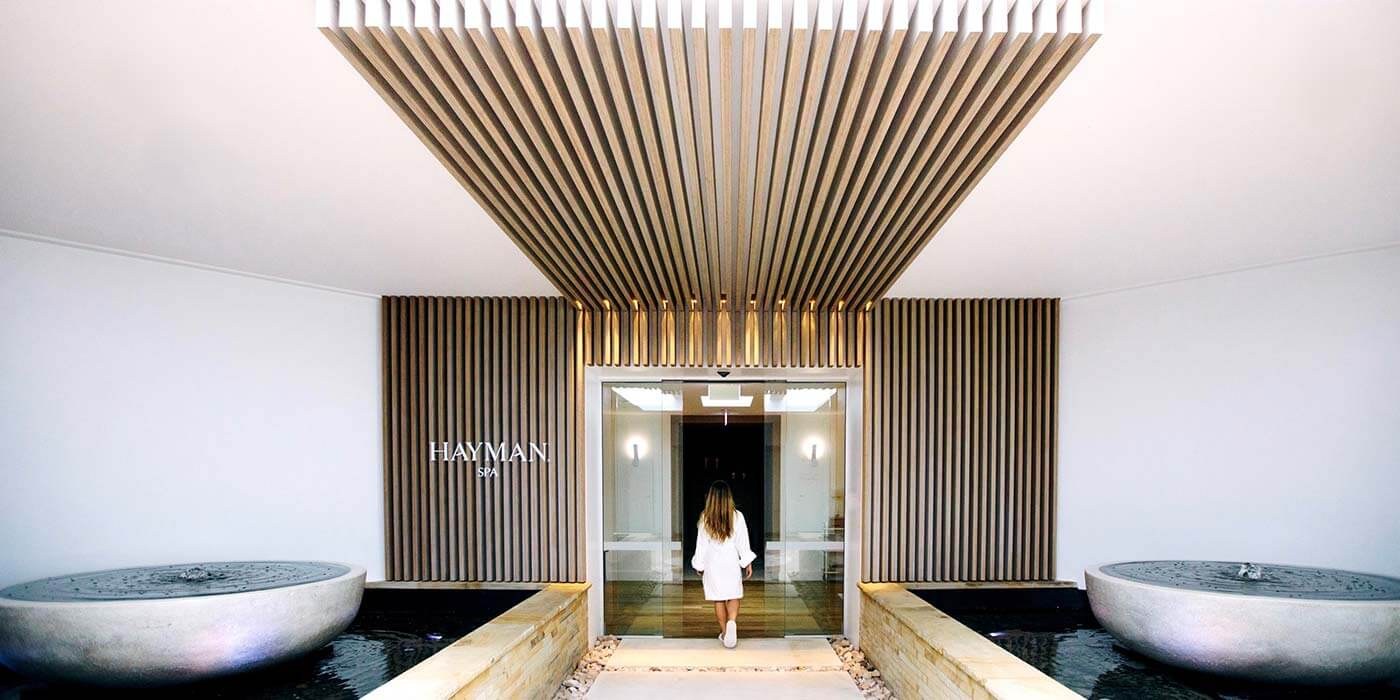 A guest in a robe walks into Hayman Spa beneath a slatted timber canopy, InterContinental Hayman Island