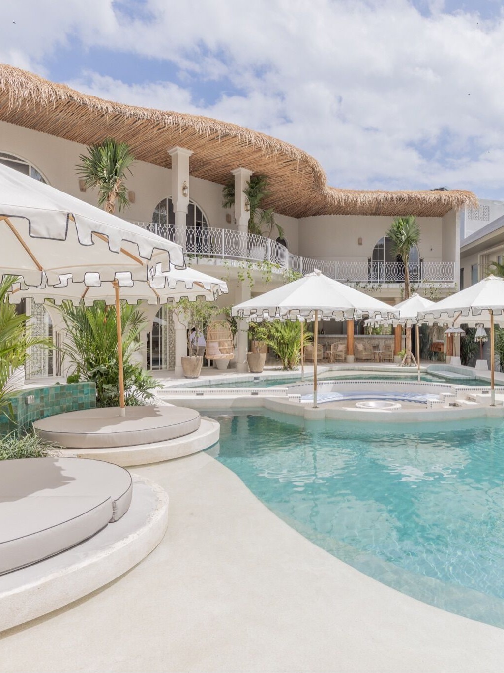 The pool at Escape Haven women's retreat in Canggu, Bali, ringed by white parasols and thatched balconies