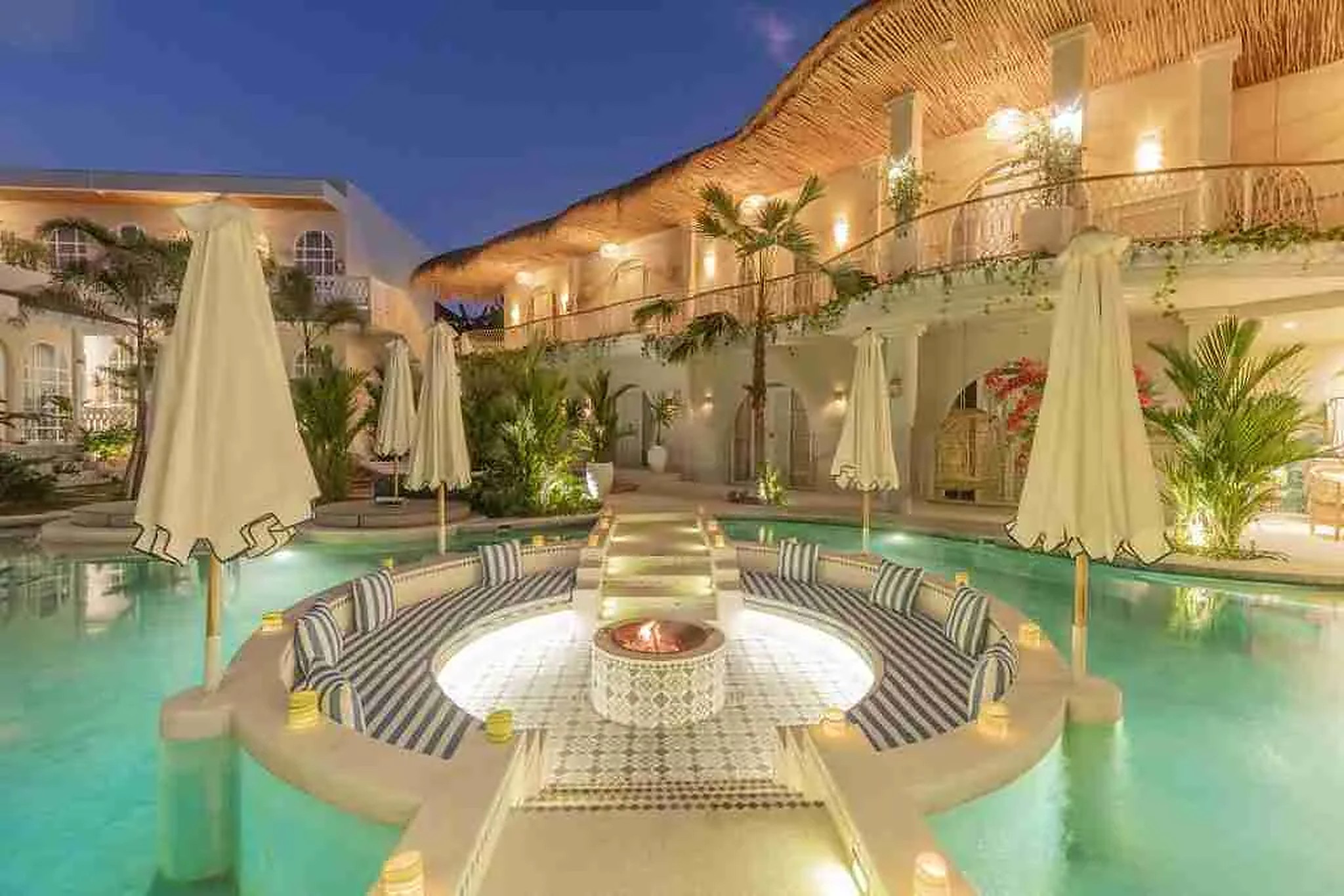 The pool at Escape Haven women's retreat in Canggu, Bali, ringed by white parasols and thatched balconies