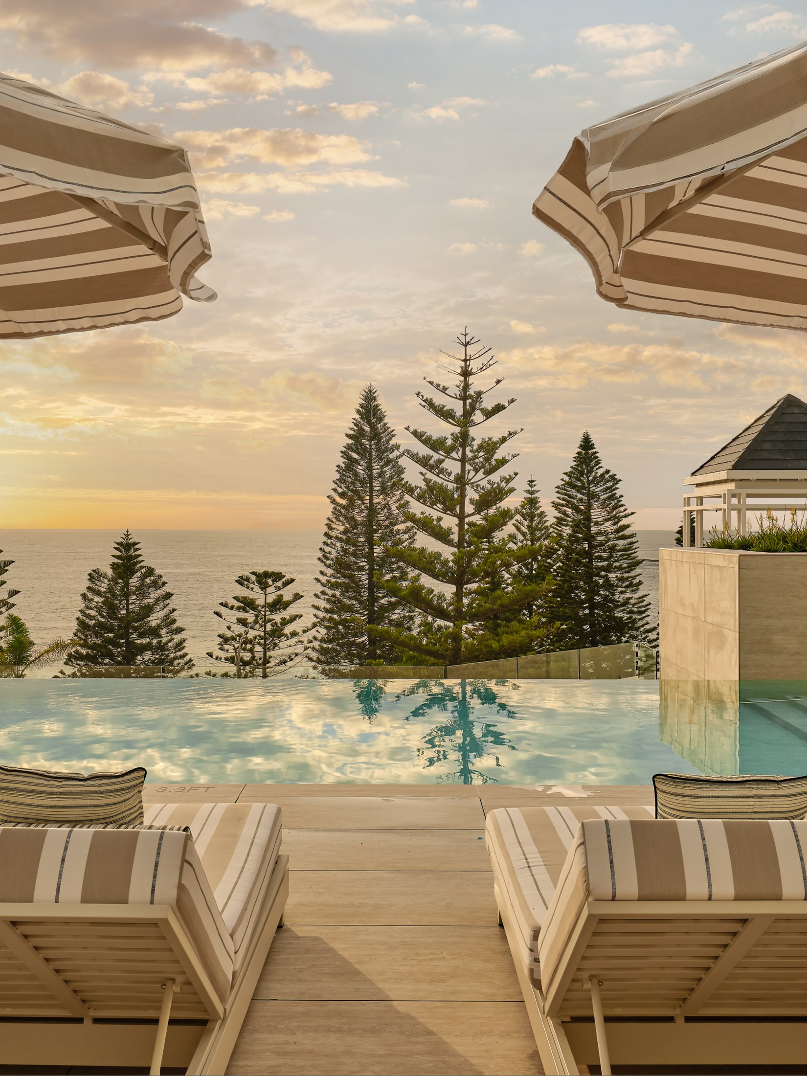 The oceanfront infinity pool at sunrise, striped umbrellas and loungers on the deck, InterContinental Sydney Coogee Beach