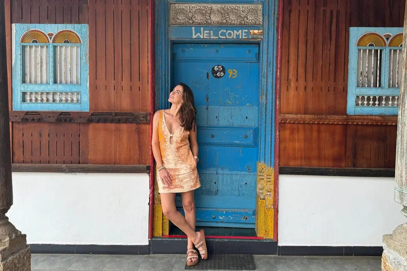 Sigourney Cantelo leaning against a blue Welcome door in Kerala, India, for Beautiful Inside by Beauticate