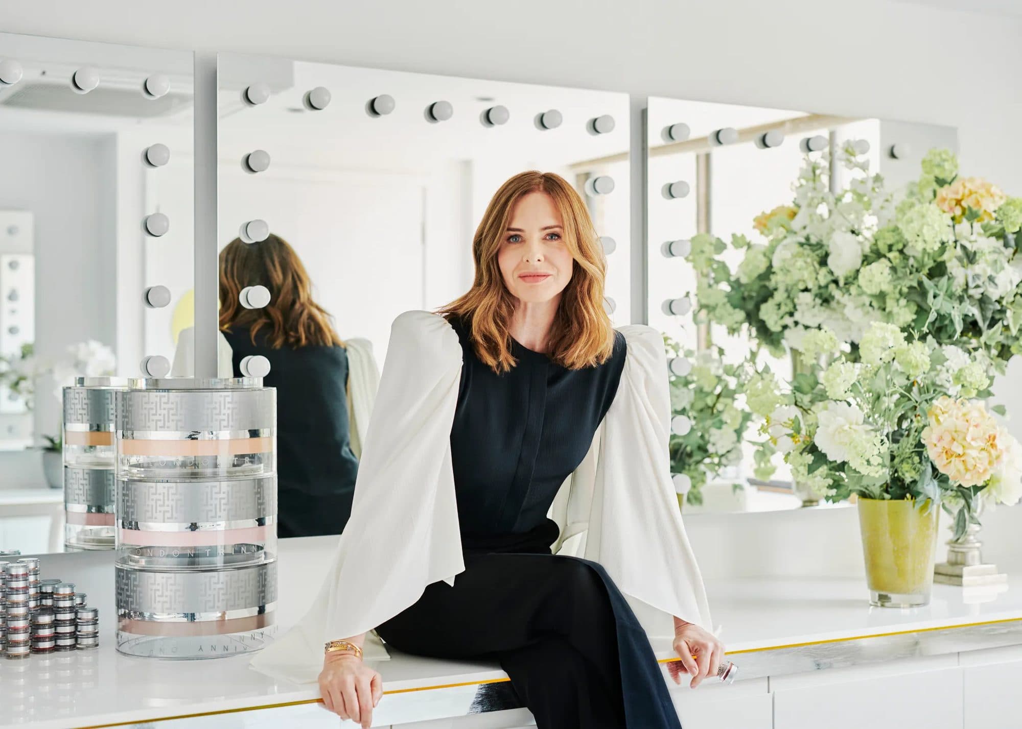 Trinny Woodall seated at her dressing table with the Trinny London stacks and fresh flowers, for Beautiful Inside by Beauticate