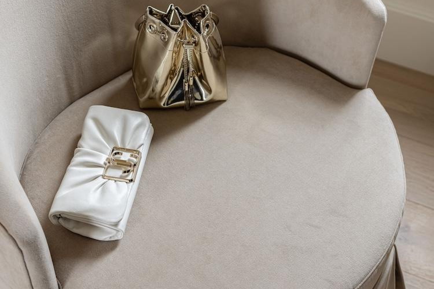 White leather clutch with gold buckle and metallic gold bucket bag on a beige velvet armchair