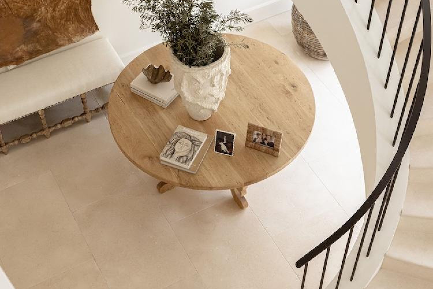 Overhead view of a round timber entry table with art books, a ceramic vase and family photos beside a spiral staircase