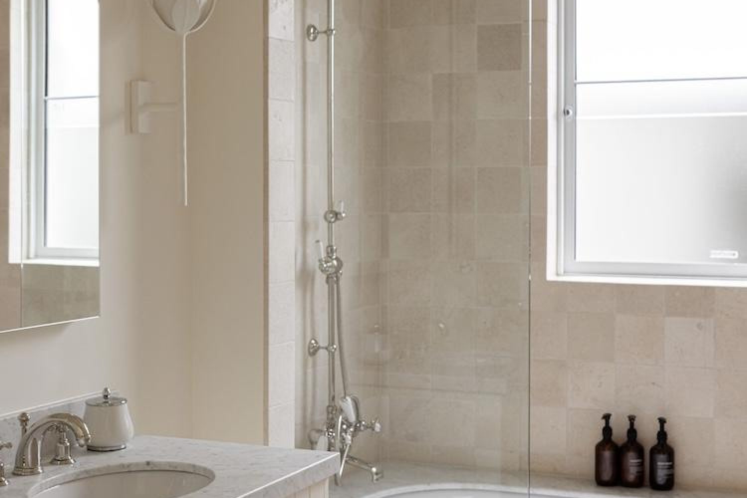 Marble bathroom with glass shower screen, chrome heritage fixtures and three brown pump bottles on a ledge
