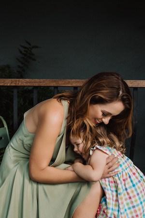 Sigourney hugging her young daughter Lulu on a verandah bench against a dark backdrop